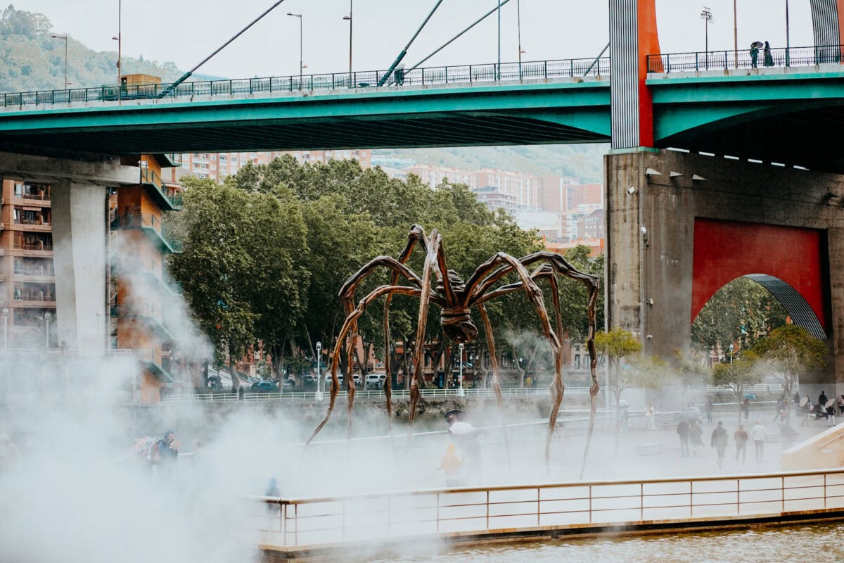 Metallic spider sculpture in the fog in front of the bridge.