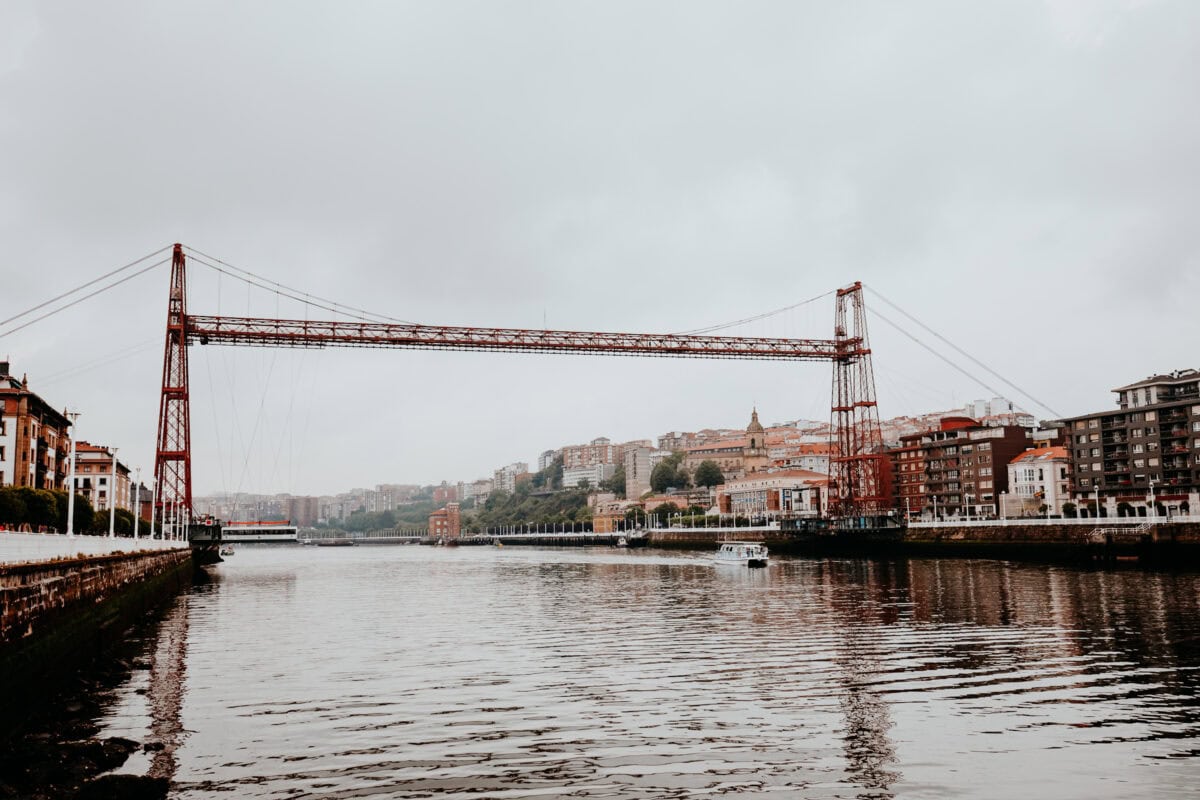 Historic suspension bridge over river in urban landscape.