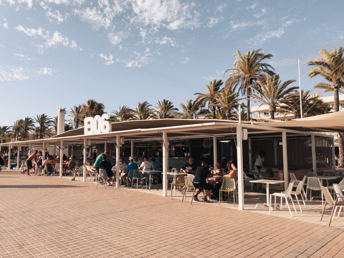 Beach bar with guests under palm trees.
