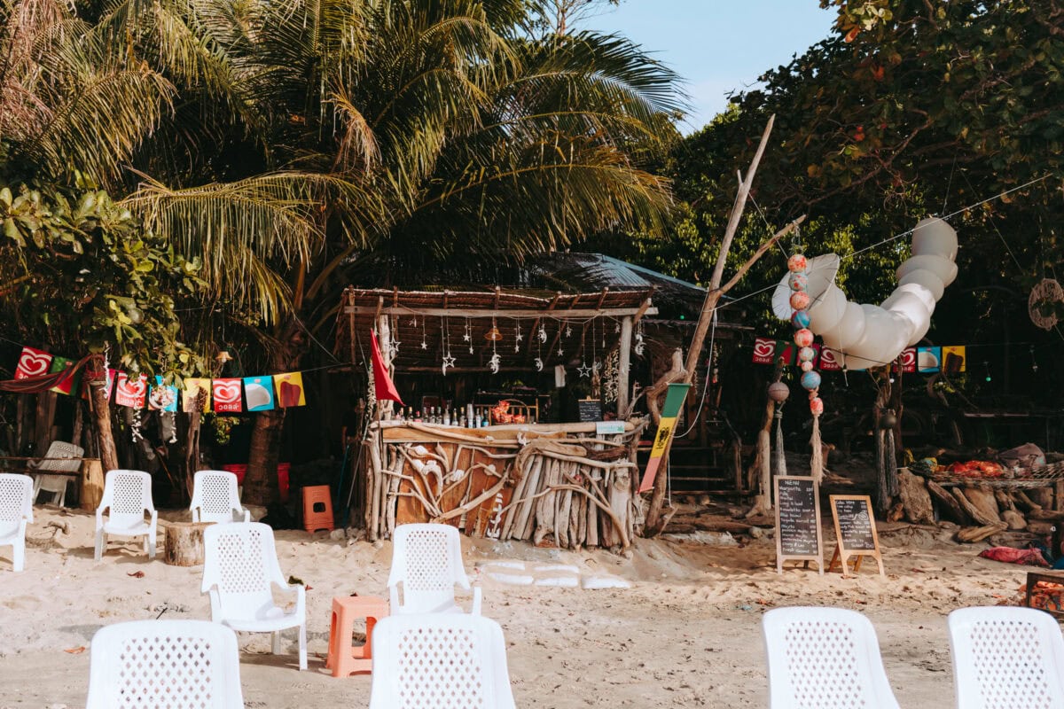 Rustic beach bar under palm trees with plastic chairs