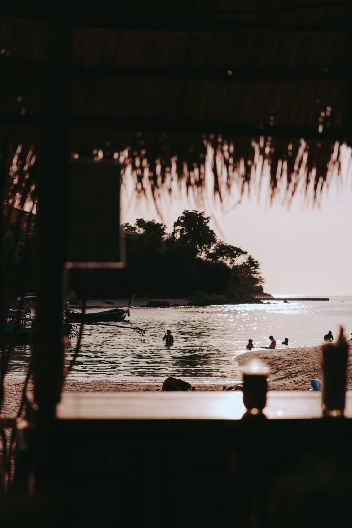 Beach at sunset with bathers and boat