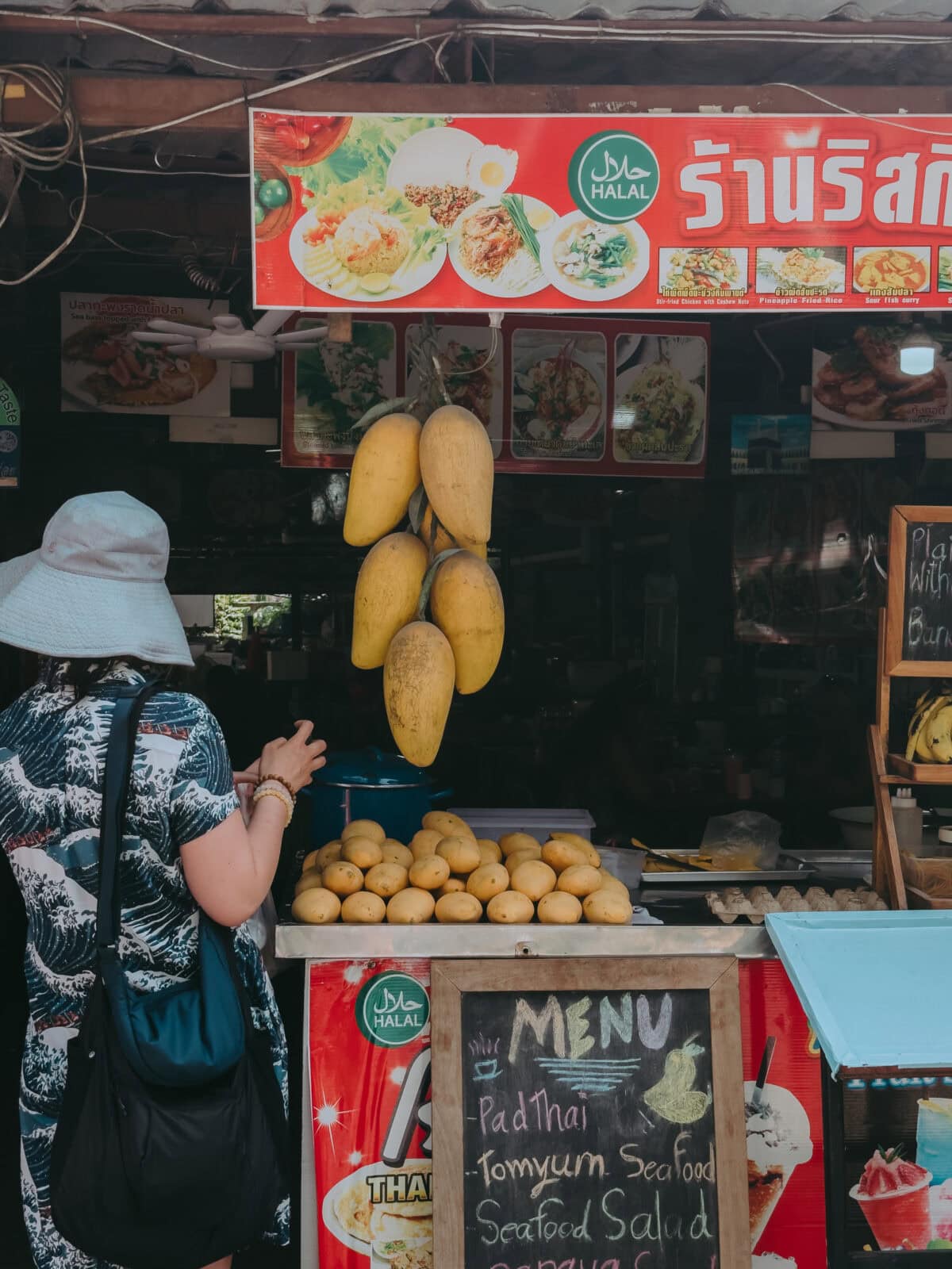 Street stall with halal sign and hanging mangoes